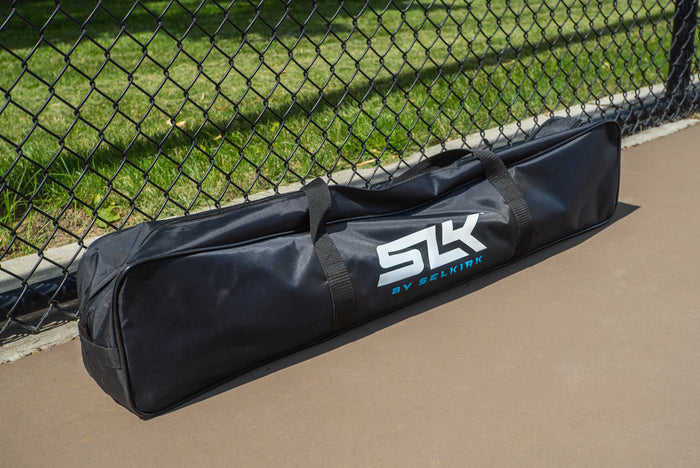 Black gear bag with white 'SLK' logo and blue 'BY SELKIRK' text, leaning against a chain-link fence.