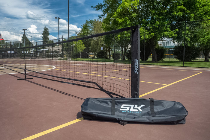 Portable SLK BY SELKIRK pickleball net and carrying bag set assembled on an outdoor court