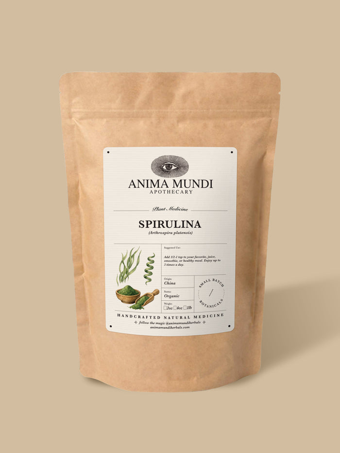 A stand-up kraft paper pouch of Anima Mundi Apothecary Spirulina powder, featuring a white label with botanical illustrations, set against a solid beige background.