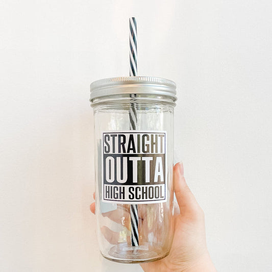 Hand holding mason jar tumbler that reads in bold black and white text straight outta high school. Reusable black and white striped straw and silver straw lid.