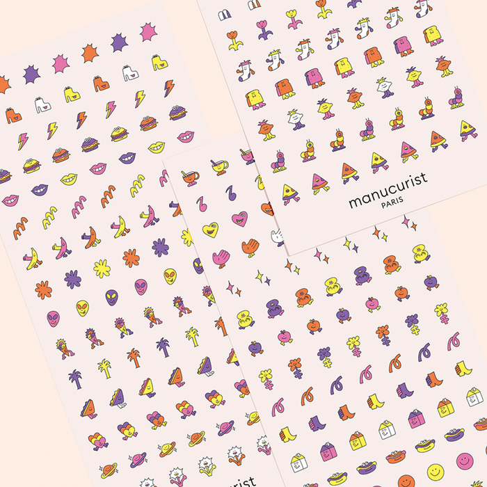 Manucurist's Summer Nail Art Stickers include three sheets of playful icons—hearts, lips, flowers, smiley faces, fruit, sunglasses, and lightning bolts—arranged in neat rows on a light background for a fun manicure.