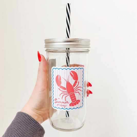 Hand holding mason jar tumbler that reads summer vibes in red ink with lobster design on pale pink and white striped background with blue border