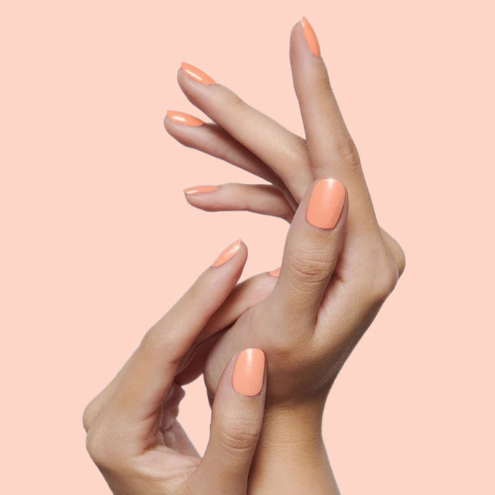 The Bold Mama Set showing hands with bright coral orange manicure on smooth nails against soft peach background