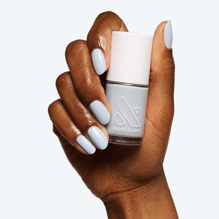 Hand with soft gray polish holding matching Olive and June nail polish bottle from The Classic Mama Set
