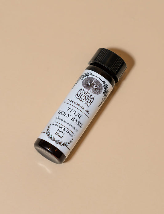 Small bottle of Tuisi Holy Basil oil with a black cap on a beige background