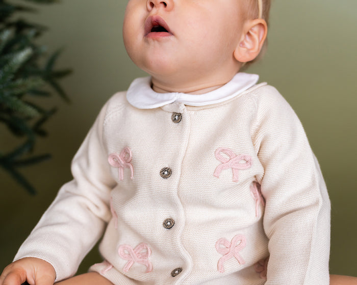 Viverano Organics baby cardigan in cream with pink bow details and button closure on a baby